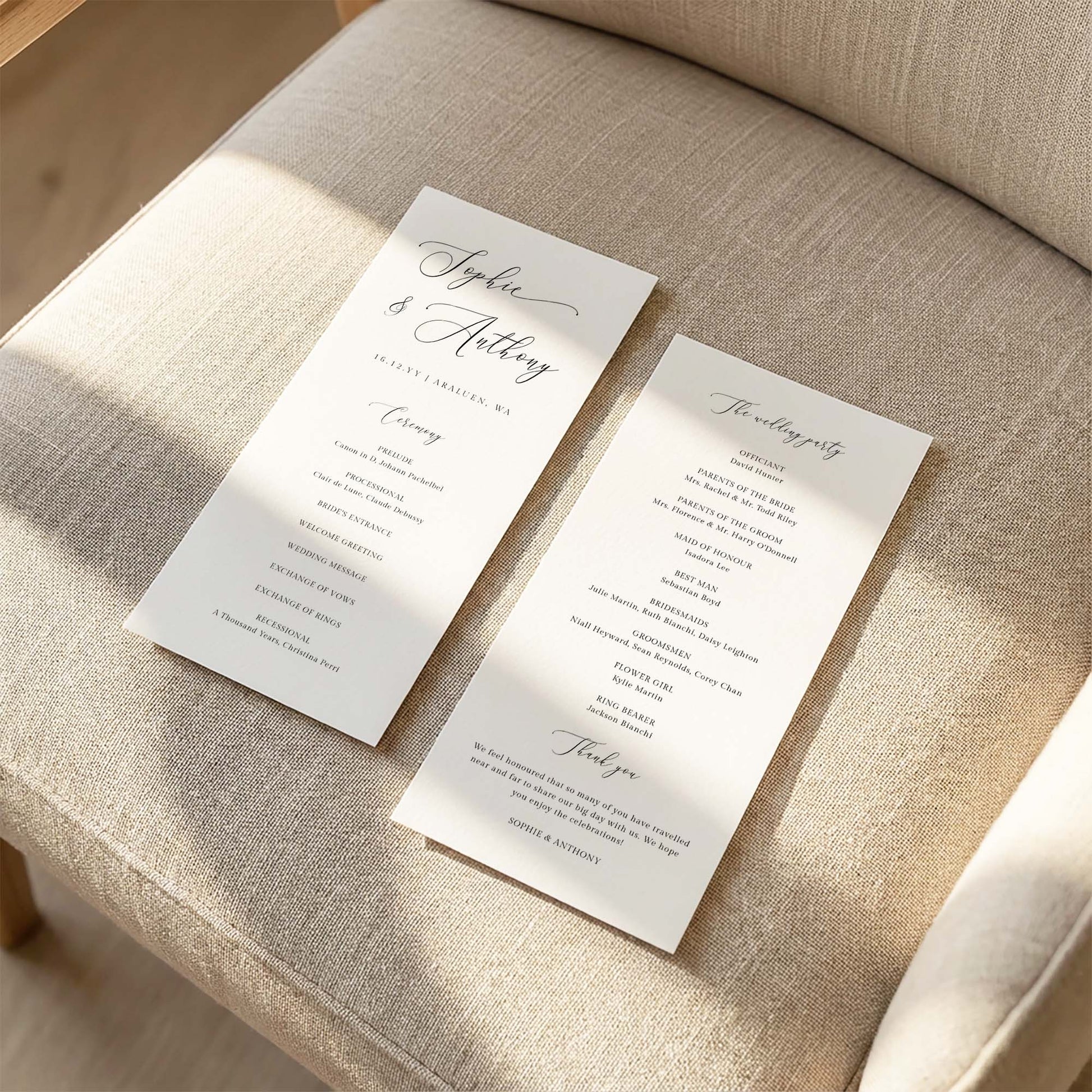 Two DL-sized wedding program cards laid flat on a cushioned chair with sunlight streaming across the linen fabric.