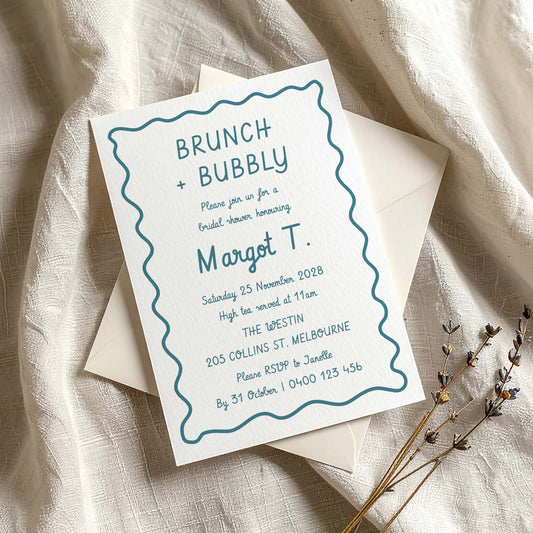 Whimsical hand-drawn bridal shower invitation template on textured card with envelope on fabric background.
