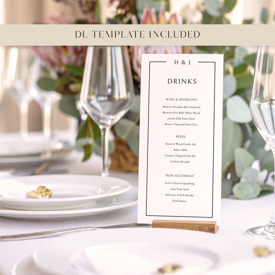 Wedding bar menu card with drink options on a wooden holder sitting on a white table cloth with flowers, plates and wine glasses.