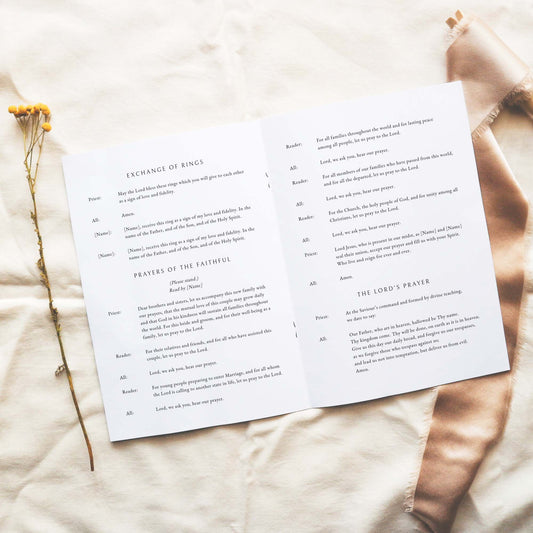 Open A5 wedding Mass ceremony booklet displaying interior ceremony text on a neutral fabric background.