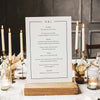 Wedding menu card on a wooden stand with candles and flowers in the background.