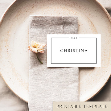 A flat place card with a name printed on it, positioned on a plate with a napkin and a floral decoration.