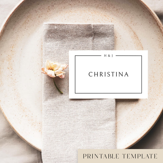 A flat place card with a name printed on it, positioned on a plate with a napkin and a floral decoration.