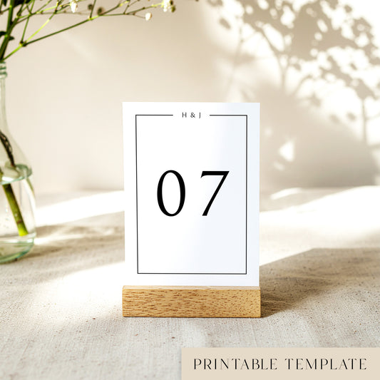 A printable table number template displayed on a small wooden block holder on a table with decorative items in the background.