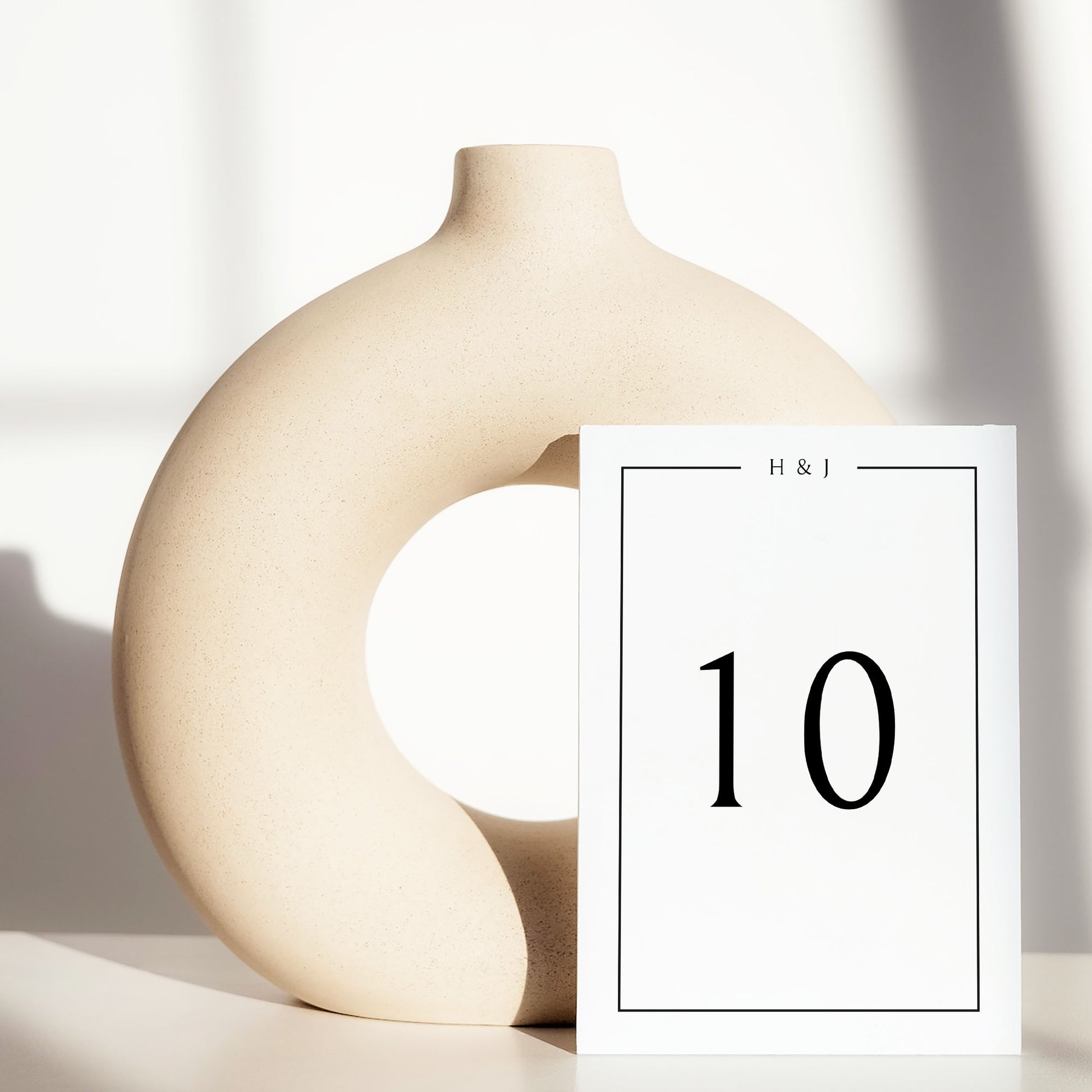 Beige ceramic circle vase with a white card displaying a table number on a light background.