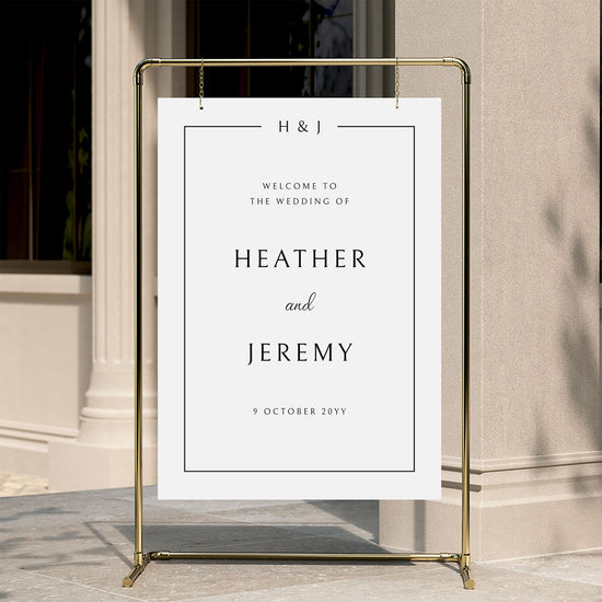 Minimal wedding welcome sign displayed on a gold stand against a neutral wall.