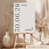 Modern typographic wedding welcome sign from the Palais collection, displayed on a wooden easel. Features a unique vertical date layout and minimalist editorial styling. DIY printable A1 poster template by The Hello Bureau.