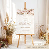 Bridal shower welcome sign with pink floral design on an easel with floral decorations and dried plants.