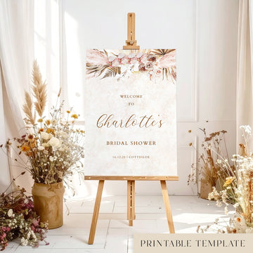 Bridal shower welcome sign with pink floral design on an easel with floral decorations and dried plants.