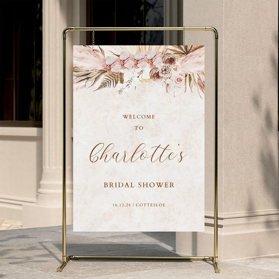 Floral bridal shower welcome sign on a stand against a neutral wall.