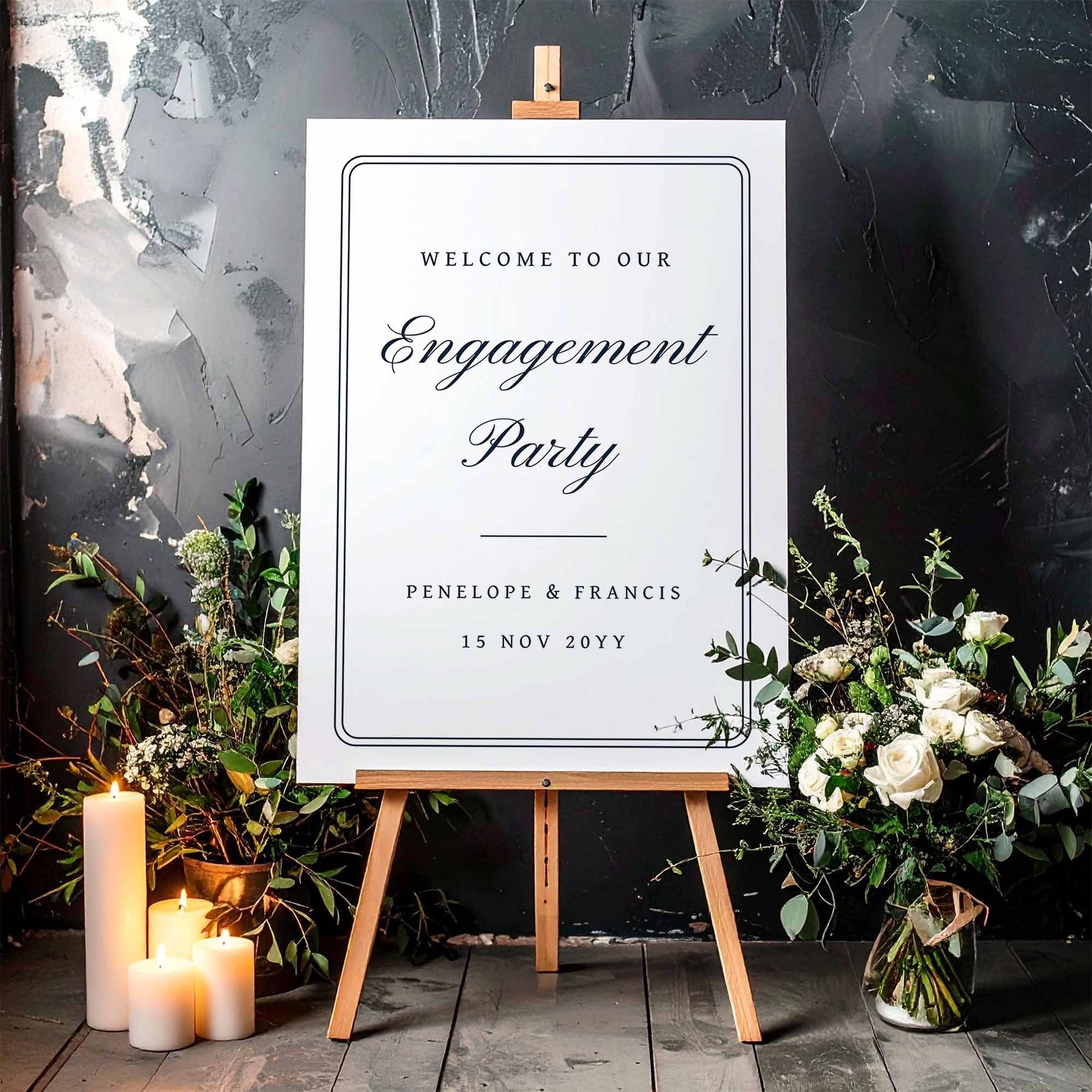 Engagement party sign on an easel with floral decorations and candles against a dark background.