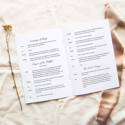 Open A5 wedding Mass ceremony booklet displaying interior ceremony text on a neutral fabric background.
