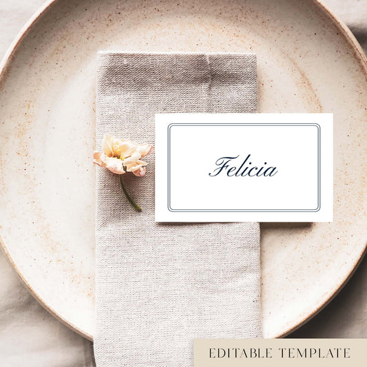 A flat place card with a border and name printed on it, positioned on a plate with a napkin and a floral decoration.