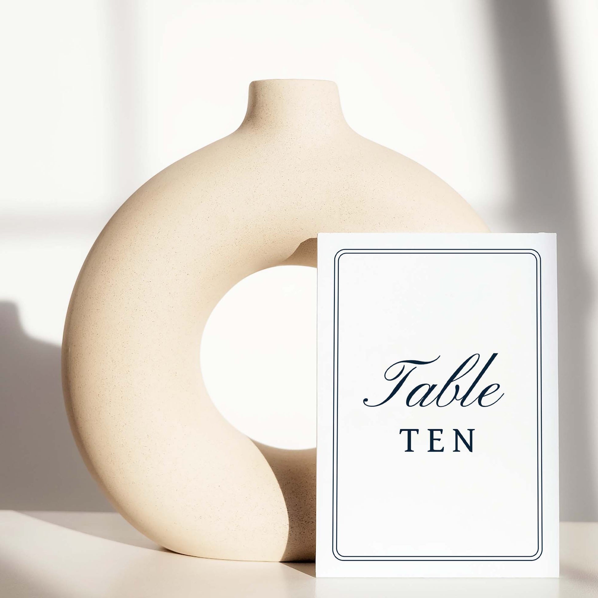 Beige ceramic circle vase with a white card displaying a table number on a light background.