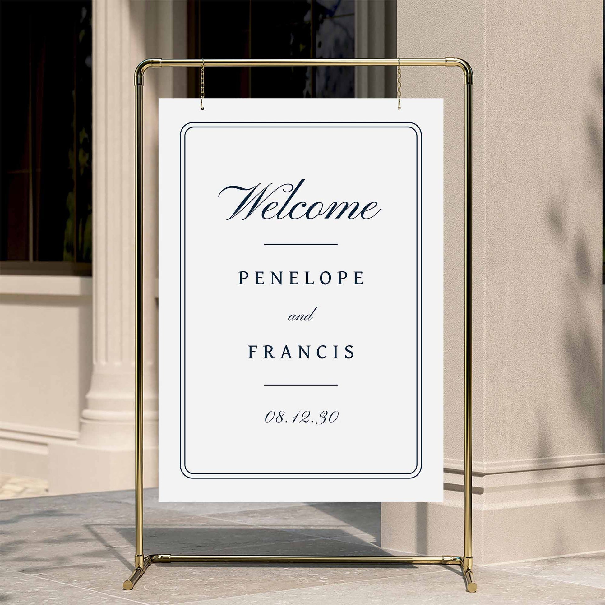 Heritage wedding welcome sign displayed on a gold stand against a neutral wall.