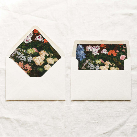 DIY fine art wedding envelope liners in a euro flap and a straight flap, with painted white, blue and pink garden flowers on deep green leaves, for 5x7 wedding invitations.