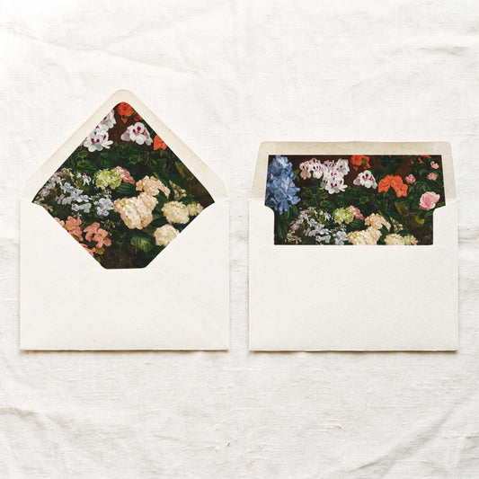 DIY fine art wedding envelope liners in a euro flap and a straight flap, with painted white, blue and pink garden flowers on deep green leaves, for 5x7 wedding invitations.