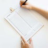 Person holding a printable day planner with a pen on a light clipboard.