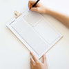 Person holding a printable day planner with a pen on a light clipboard.