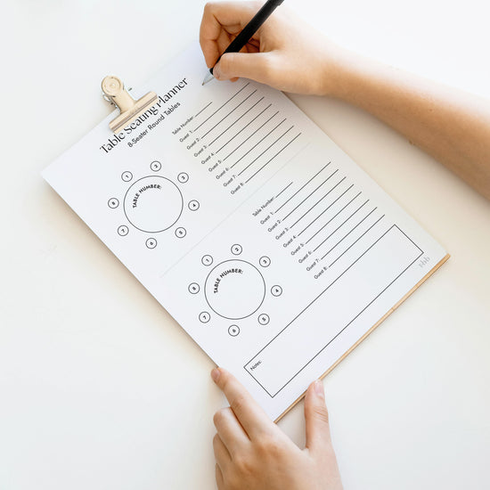 Person holding a table seating chart planner on a clipboard.