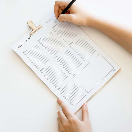 Weekly to-do list on a clipboard with hands holding a pen, on a light background.