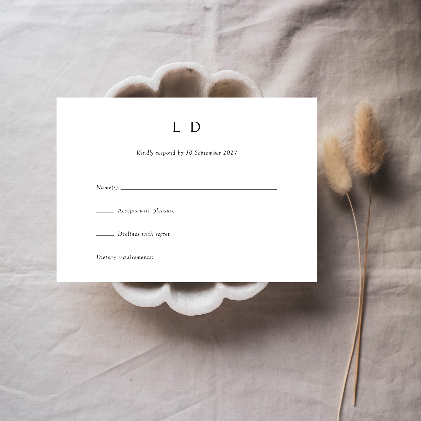 A minimalist horizontal wedding invitation RSVP card on a plate next to two flowers.