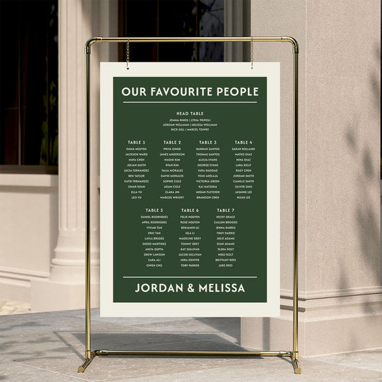 DIY bold forest green wedding seating chart template hanging from a gold frame at a modern city venue.