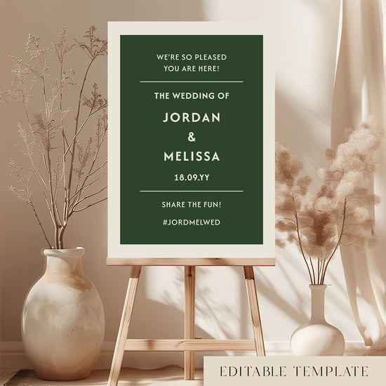 DIY wedding welcome sign template in forest green and cream displayed on a wooden easel. Features the Renard minimalist design in a bright, modern room with dried botanicals. Printable A1 or A2 size by The Hello Bureau.