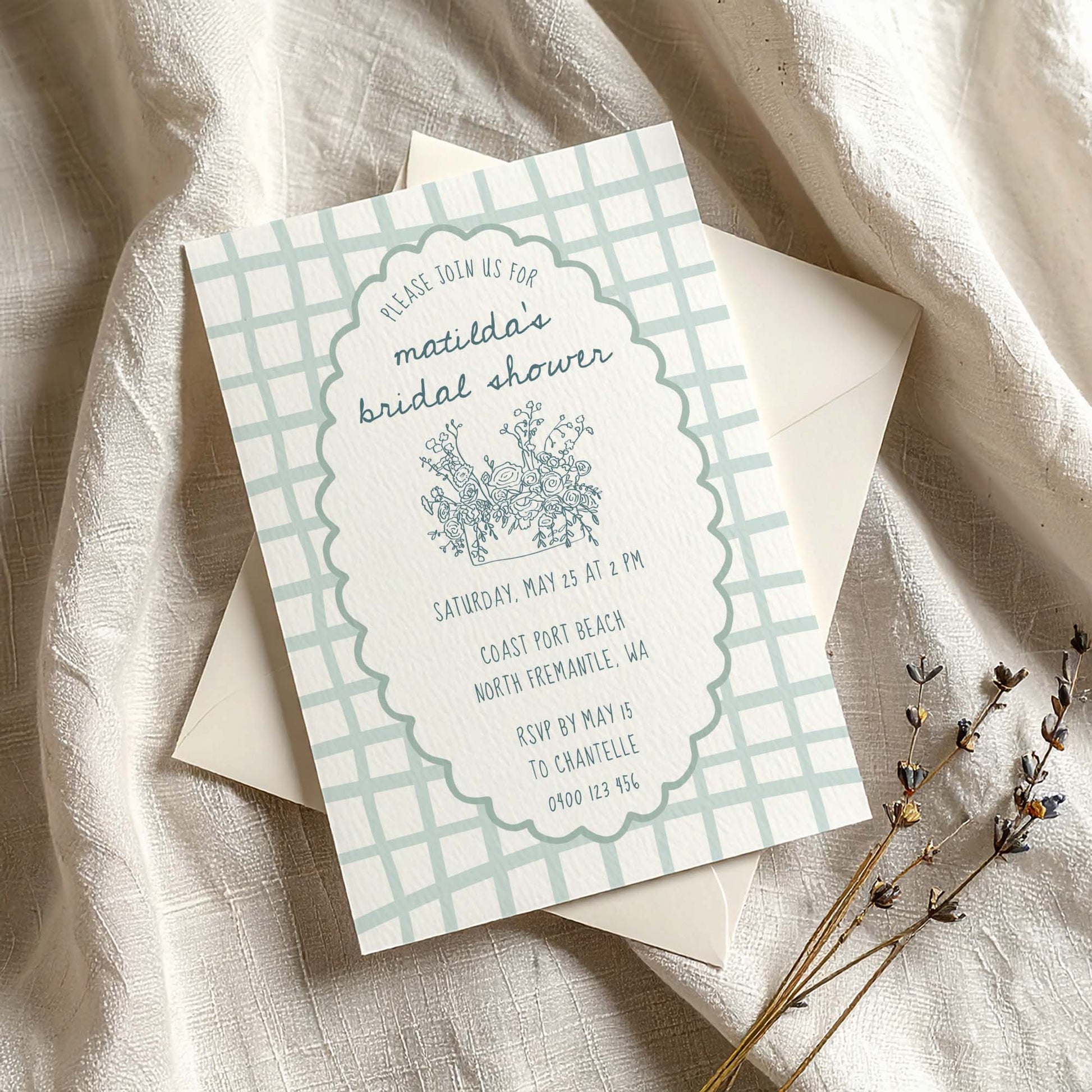 Whimsical blue bridal shower invitation on textured card with envelope on fabric background.