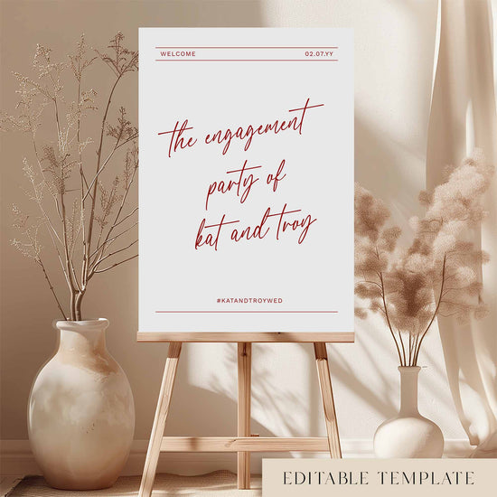 Modern red engagement party welcome sign on an easel with floral arrangements in a room setting.