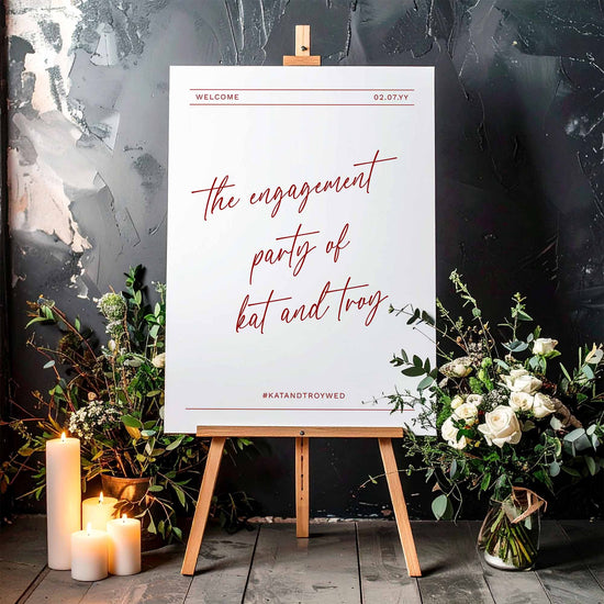 Engagement party sign on a wooden easel, surrounded by flowers and candles.