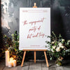 Engagement party sign on a wooden easel, surrounded by flowers and candles.