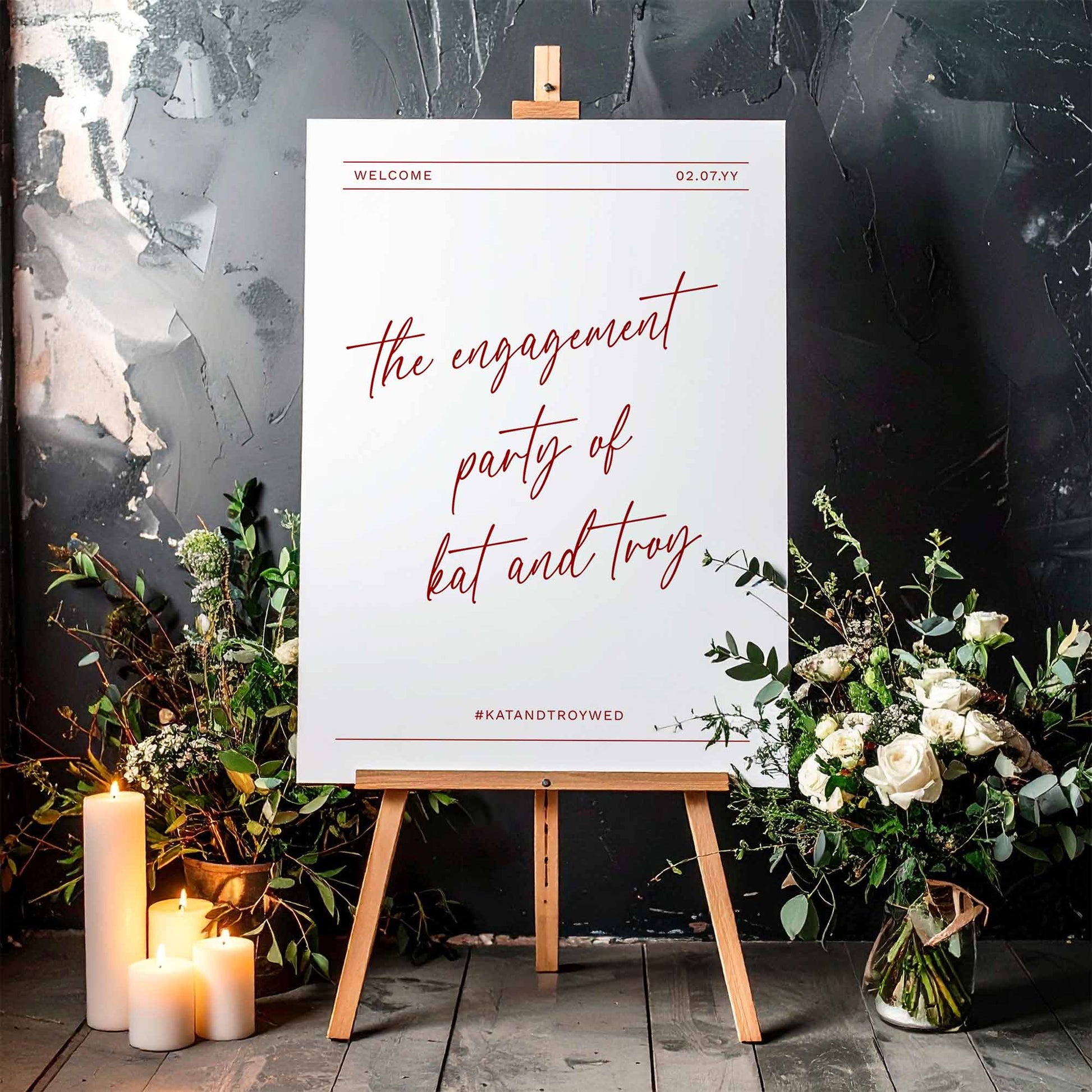 Engagement party sign on a wooden easel, surrounded by flowers and candles.