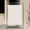 Alphabetical wedding seating chart template displayed on a gold stand against a neutral wall.