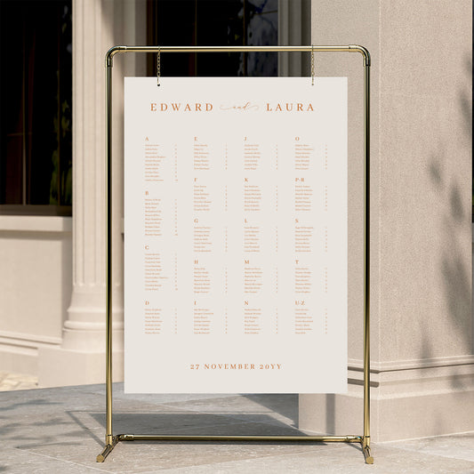 Alphabetical wedding seating chart template displayed on a gold stand against a neutral wall.