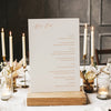 Wedding menu card on a wooden stand with candles and flowers in the background.
