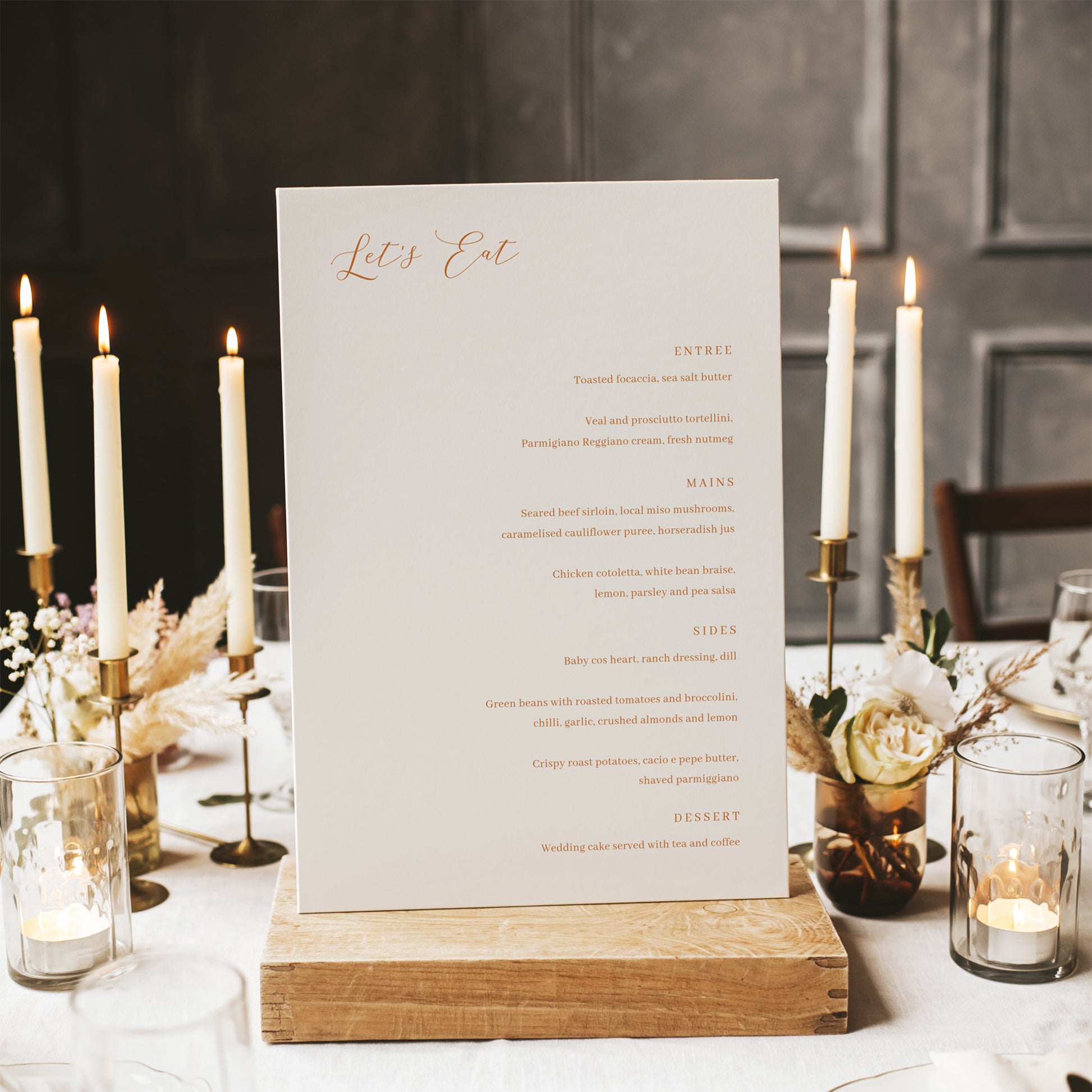 Wedding menu card on a wooden stand with candles and flowers in the background.