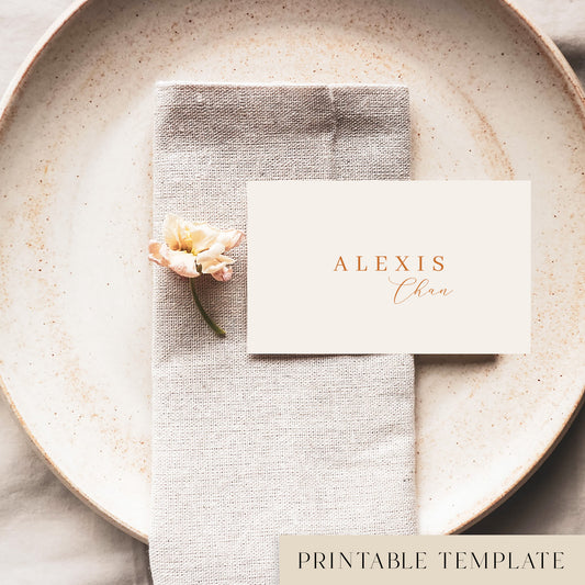 A flat place card with a name printed on it, positioned on a plate with a napkin and a floral decoration.