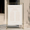 Minimal wedding seating chart template displayed on a gold stand against a neutral wall.