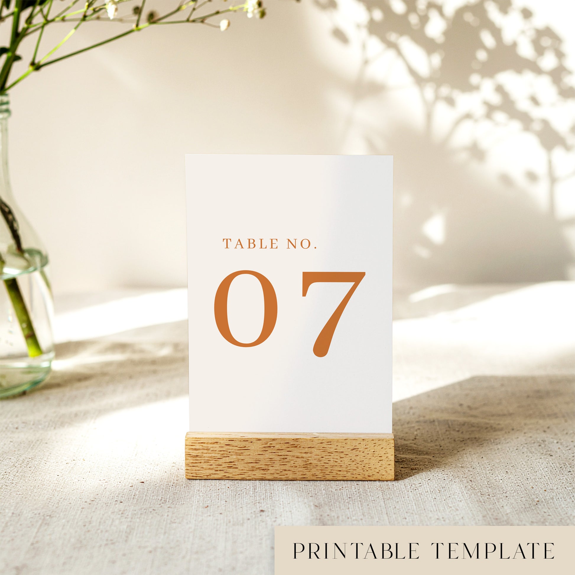 A printable table number template displayed on a small wooden block holder on a table with decorative items in the background.