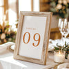 Printable table number card displayed on a wooden stand on a linen table cloth.