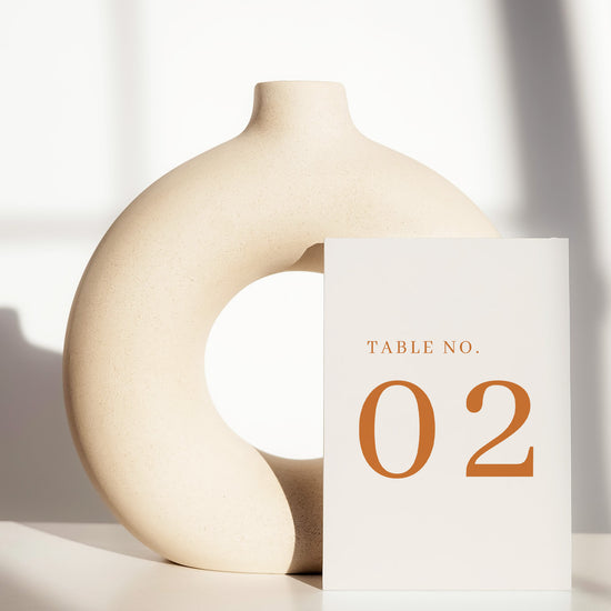 Beige ceramic circle vase with a white card displaying a table number on a light background.