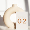 Beige ceramic circle vase with a white card displaying a table number on a light background.