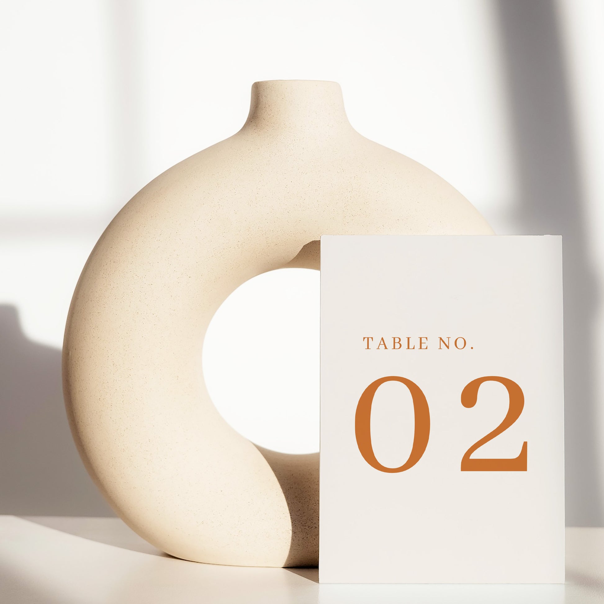 Beige ceramic circle vase with a white card displaying a table number on a light background.