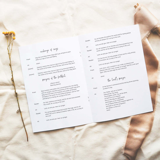 Open A5 wedding Mass ceremony booklet displaying interior ceremony text on a neutral fabric background.