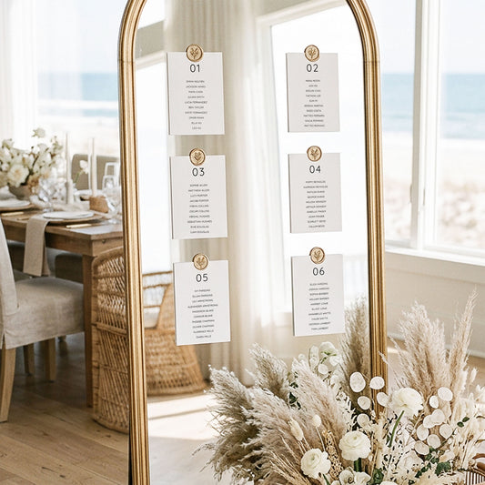 Wedding mirror table plan display with six printable minimal table cards attached with gold wax seals in an elegant light-filled coastal venue.