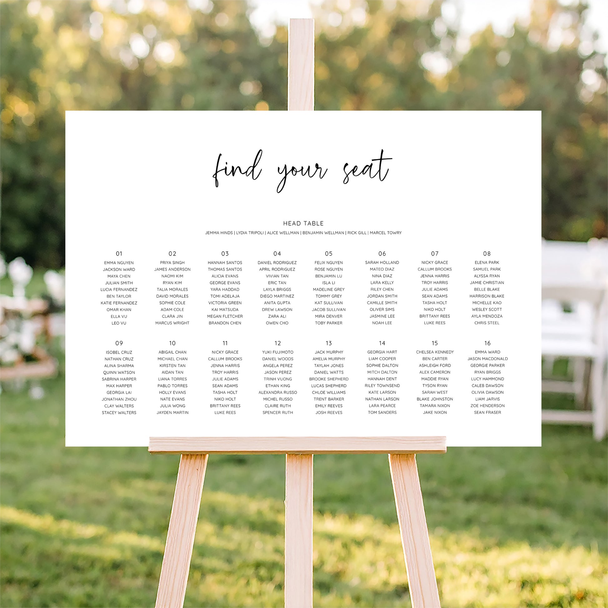 Horizontal wedding seating plan sign on an easel with a blurred outdoor ceremony background.