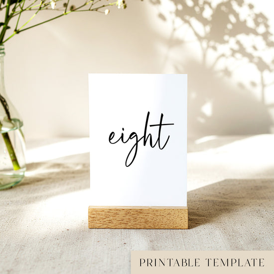 Printable table number card displayed on a wooden stand on a linen table cloth.