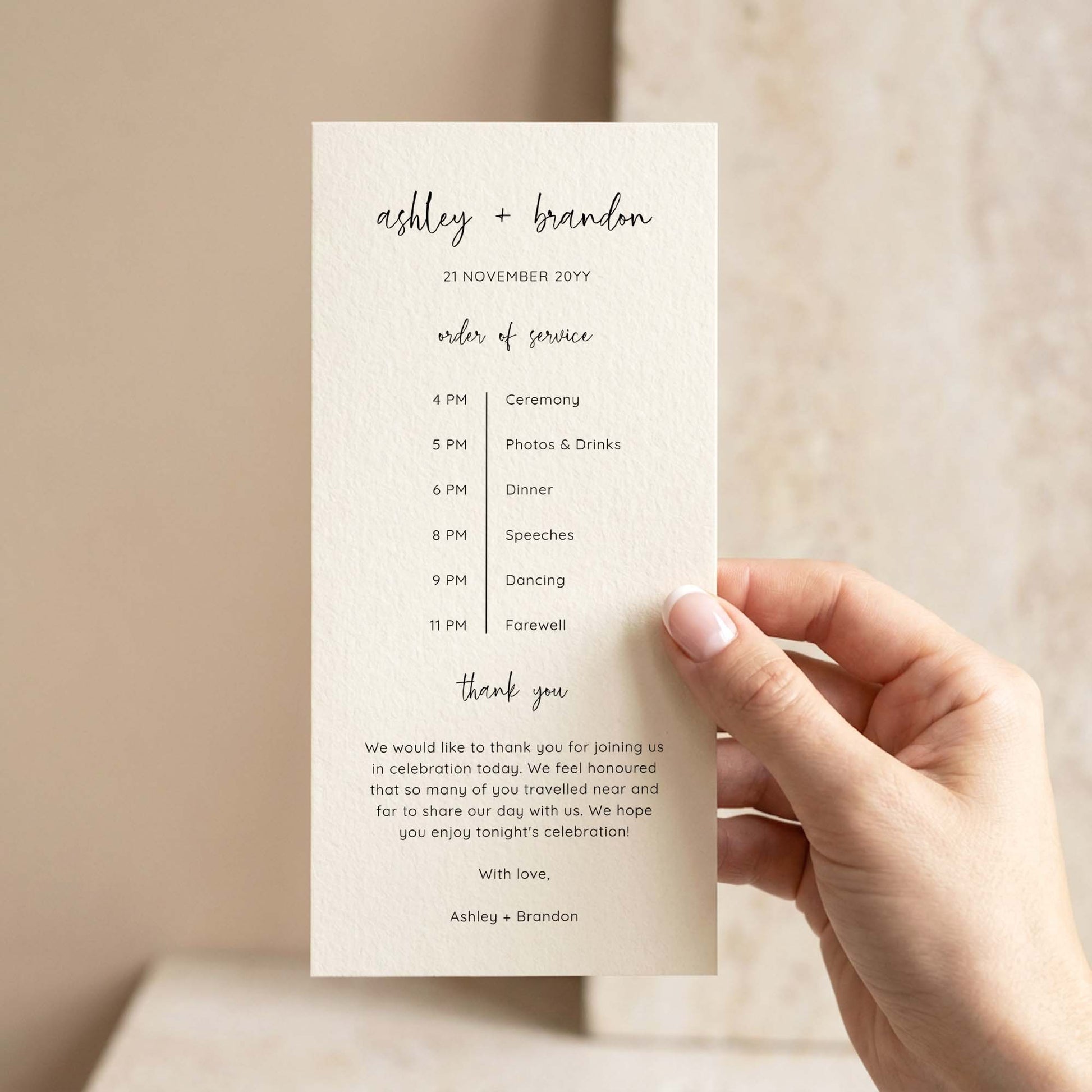 A hand holding a single DL-sized wedding program card in front of a softly lit neutral background.