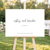 Horizontal wedding welcome sign on an easel with a blurred outdoor ceremony background.